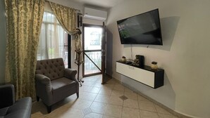 A living room with a sofa, a TV mounted on the wall, and a balcony door. - Central Hacienda 5 min from the beach and the famous 5th ave with swimming pool (Playa del Carmen)