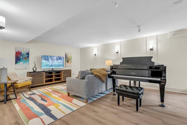 A living room with a grand piano, a sofa, a television, and a colorful rug.