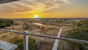 A sunset view from a balcony with a railing, a wooden dock, and a river. - Sounds Good! (Surf City)
