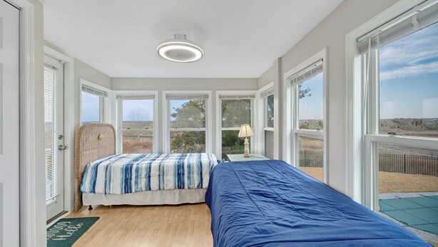 A bedroom with two beds, large windows, a ceiling light, and a view of the outdoors. - Sounds Good! (Surf City)