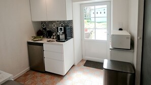 A compact kitchen with white cabinets, a coffee machine, and a small refrigerator.