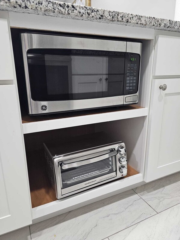 Una cocina con un microondas GE y un horno tostador Hamilton Beach sobre estantes abiertos.