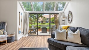 Una sala de estar con un sofá gris, una mesa de centro y vistas a un patio exterior con una mesa y sillas.