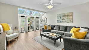 Un salón espacioso con un sofá gris, un sillón blanco, una mesa de centro y un ventilador de techo.