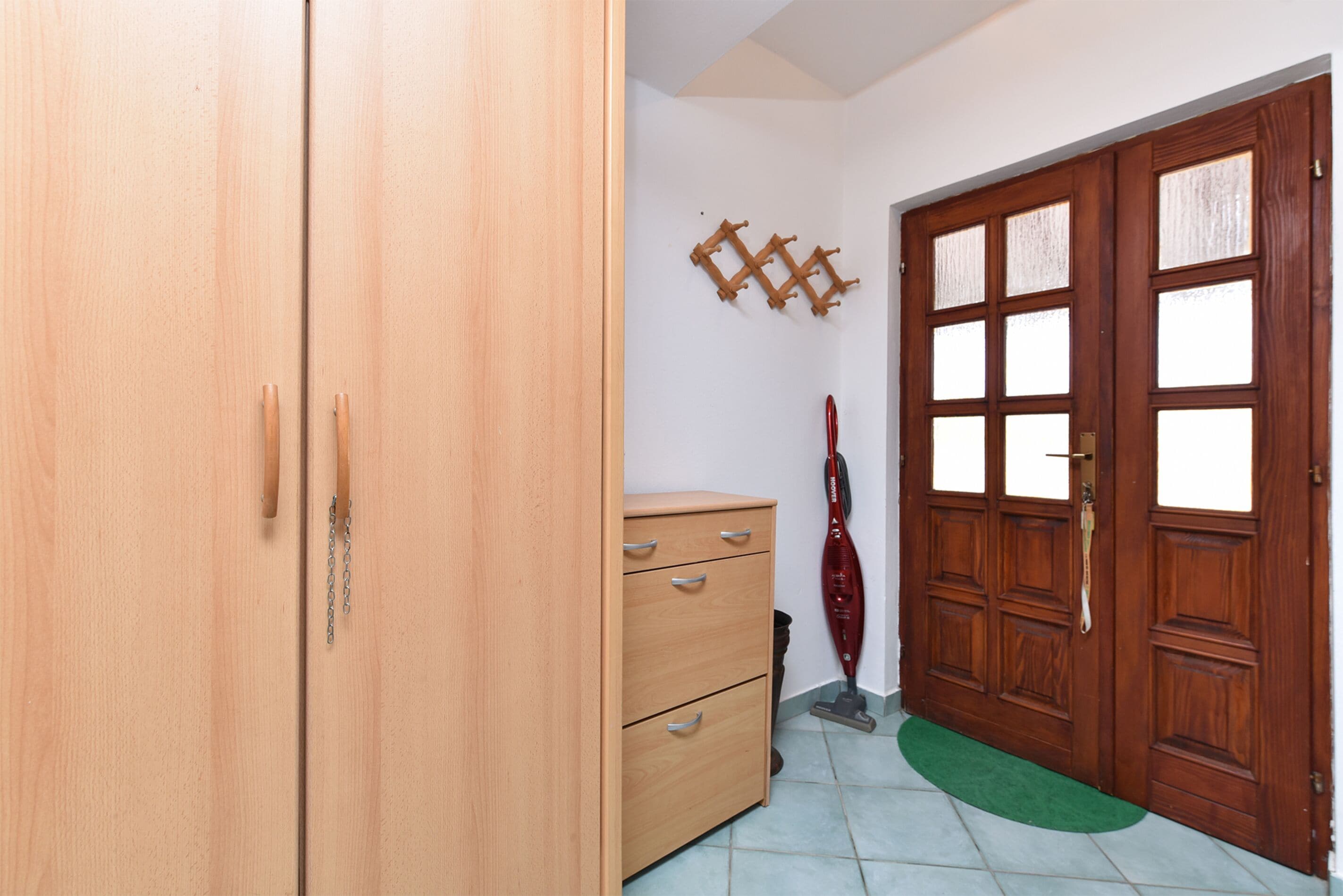 Una stanza con un'armadio in legno, una piccola credenza e una porta in legno con pannelli di vetro.