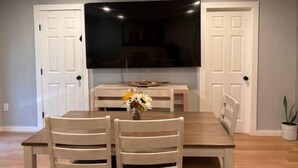A dining area with a wooden table and chairs, a flat-screen TV mounted on the wall, and a small vase with flowers on the table. - Luxury private apartment (Metairie)