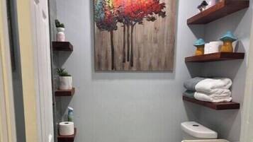 A compact bathroom with a toilet, sink, and shelves with toiletries.