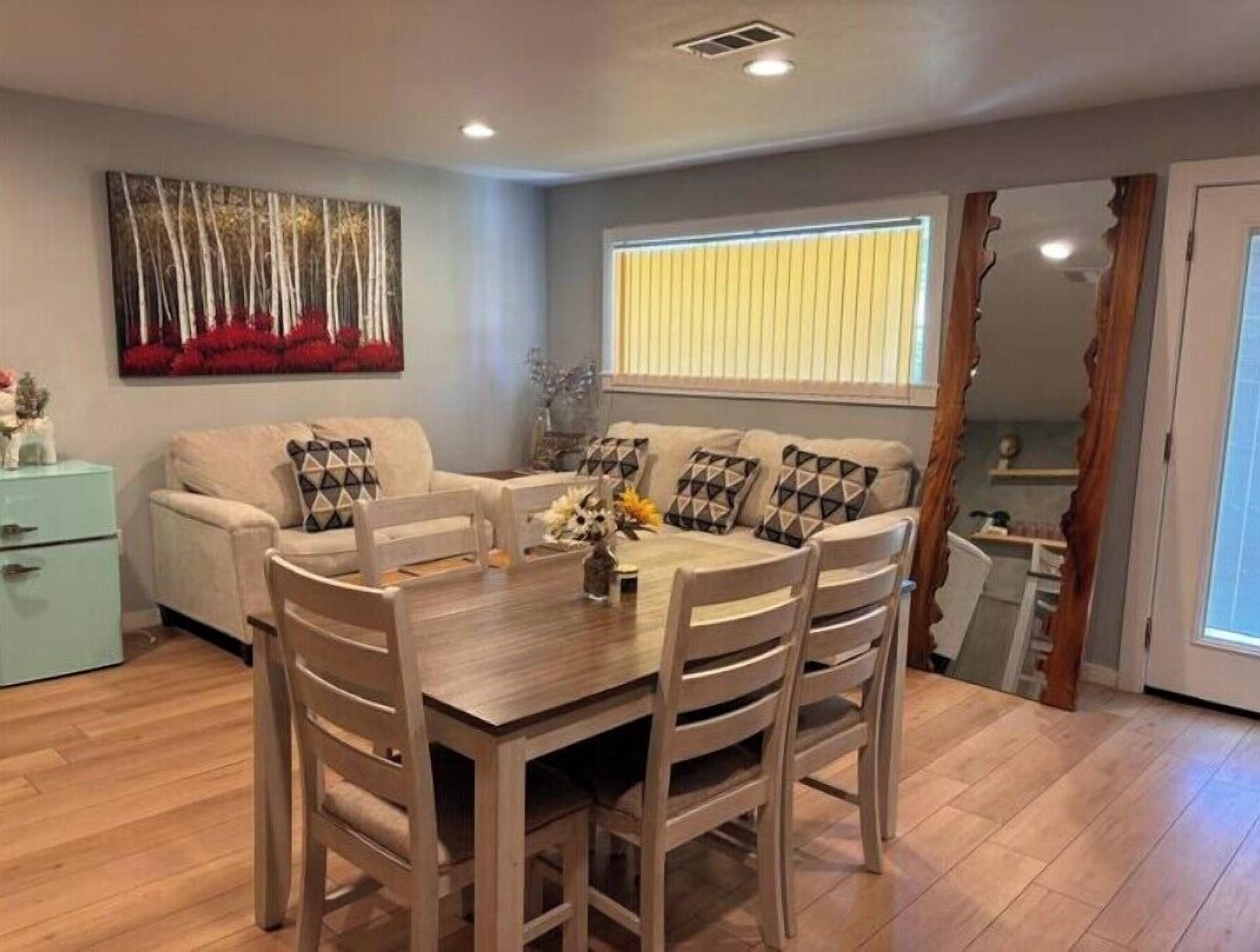 Un comedor con una mesa y sillas de madera, un sofá con cojines estampados, y un cuadro en la pared.