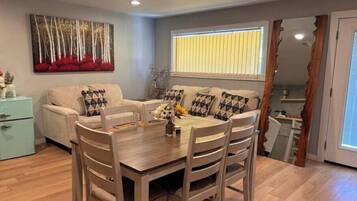 Un comedor con una mesa y sillas de madera, un sofá con cojines estampados, y un cuadro en la pared.