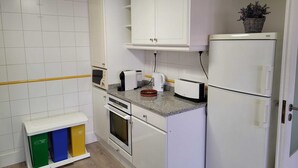 A compact kitchen with white cabinets, a microwave, a toaster, and a refrigerator.