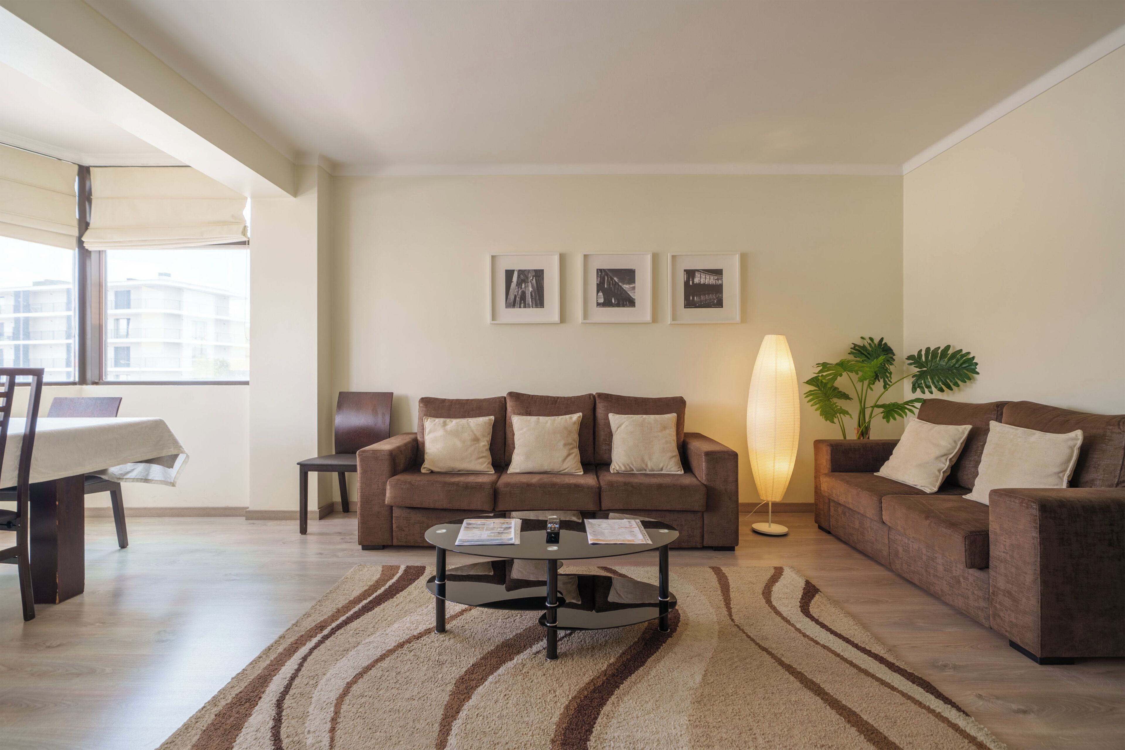 A living room with a sofa, armchairs, a coffee table, and a floor lamp. There are three framed pictures on the wall.