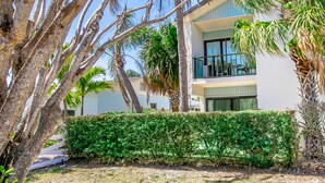 A modern two-story building with a balcony, surrounded by palm trees and a well-maintained hedge. - Cozy & Peaceful Lido Beach Condo — Steps to the Beach and St. Armands.  (Sarasota)