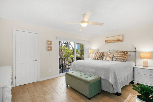 A bedroom with a bed, a ceiling fan, a nightstand, a bench, and a view of the outdoors.