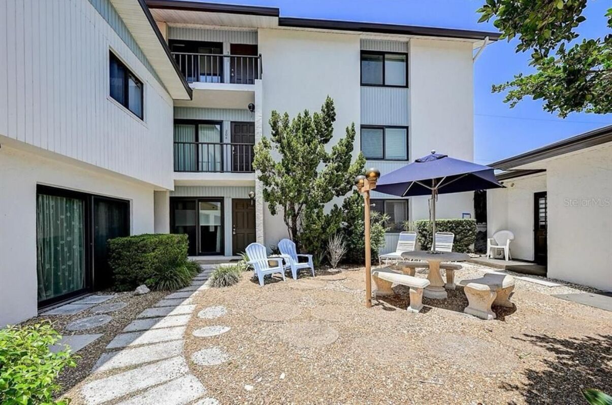 Ein mehrstöckiges Wohngebäude mit Innenhof, der Sitzgelegenheiten, eine Pergola und eine kleine Gartenanlage bietet.