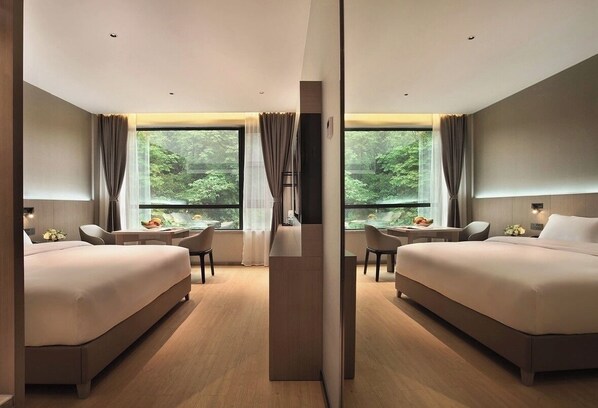 Una habitación de hotel moderna con dos camas, un escritorio y vistas a zonas verdes a través de amplios ventanales.