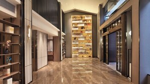 Een moderne hotelgang met een grote boekenkast in het midden, gepolijste marmeren vloeren en eigentijdse meubels.
