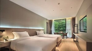 Een moderne hotelkamer met twee bedden, een zithoek en een groot raam met uitzicht op het landschap.