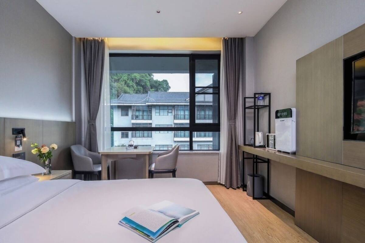 A hotel room with a bed, a desk, a chair, a TV, and a window with a view of buildings.