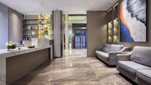 Een moderne lobby met een marmeren receptiebalie, een zithoek met banken, een boekenkast en een groot abstract schilderij.