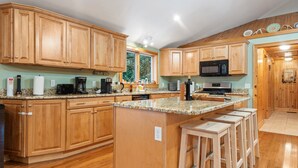 A kitchen with wooden cabinets, granite countertops, a built-in island with stools, a microwave, and a coffee machine. - Cozy 3-bedroom cabin in charming Haverhill with Hot Tub, Play Area & Fire Pit (Haverhill)