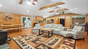 A spacious living room with a fireplace, wooden ceiling beams, and a large rug with tribal patterns. - Cozy 3-bedroom cabin in charming Haverhill with Hot Tub, Play Area & Fire Pit (Haverhill)