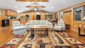 A spacious living room with a large wooden ceiling, a central coffee table, and a patterned rug. - Cozy 3-bedroom cabin in charming Haverhill with Hot Tub, Play Area & Fire Pit (Haverhill)