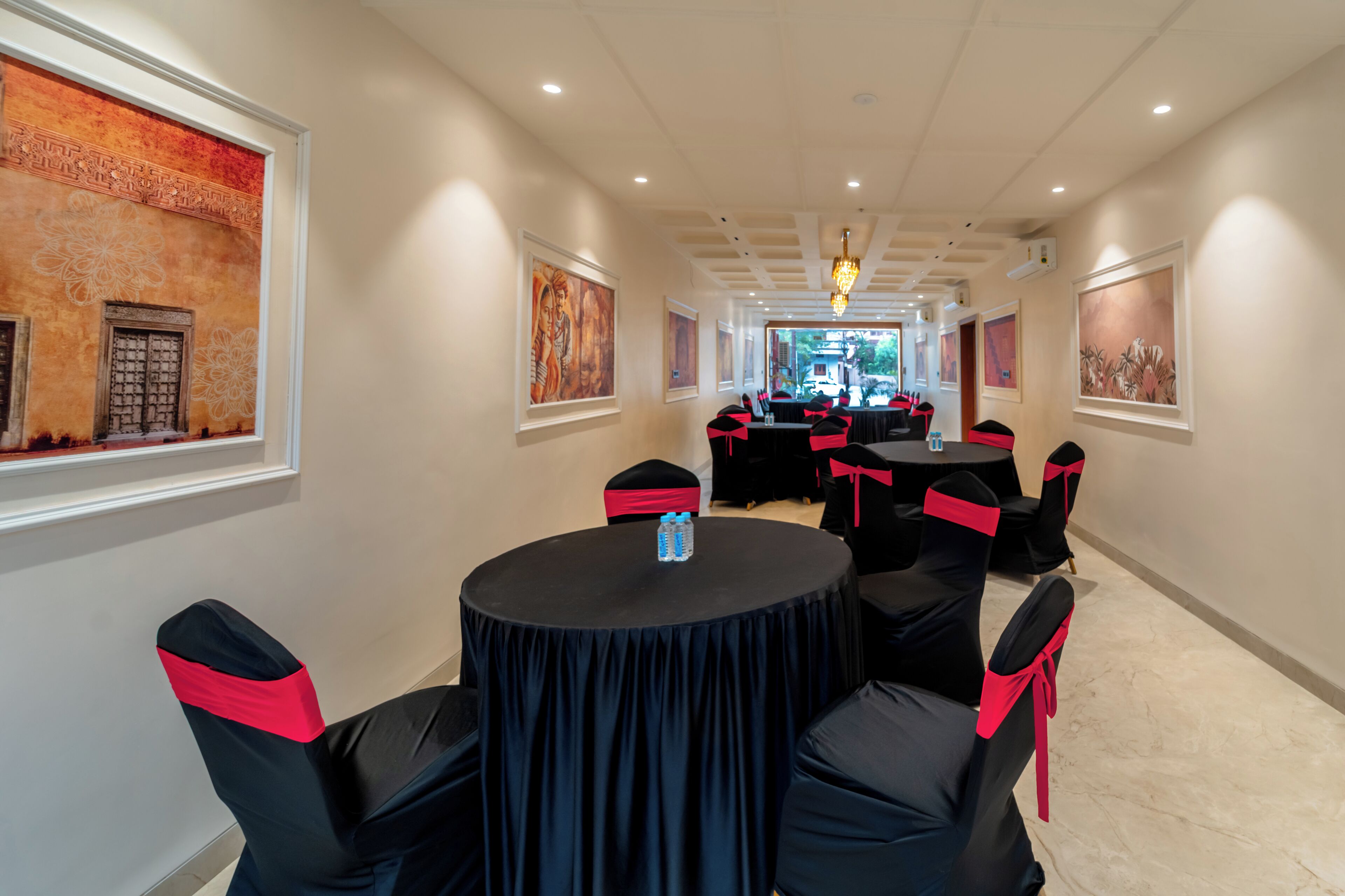 A conference room with round tables and chairs, framed artwork on the walls, and a chandelier.