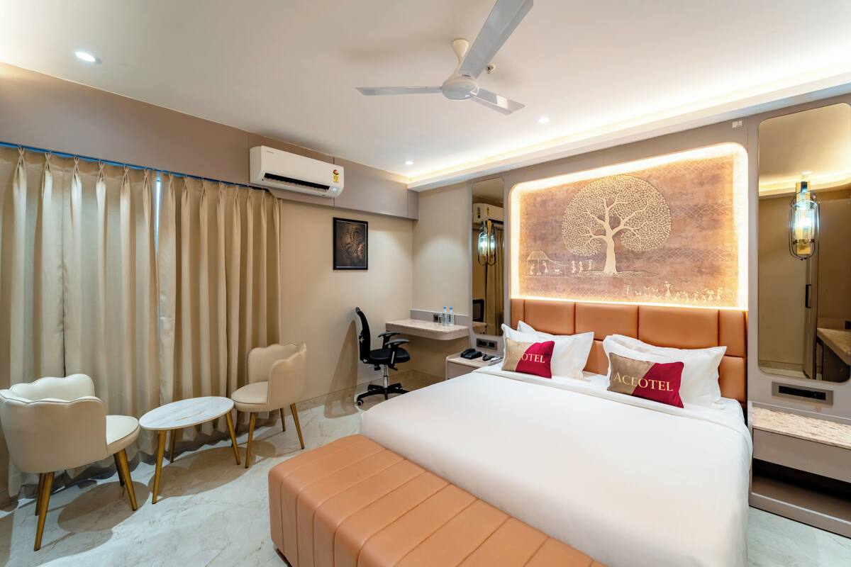 Quarto de hotel com cama, escrivaninha, cadeira, mesa pequena e ventoinha no teto.