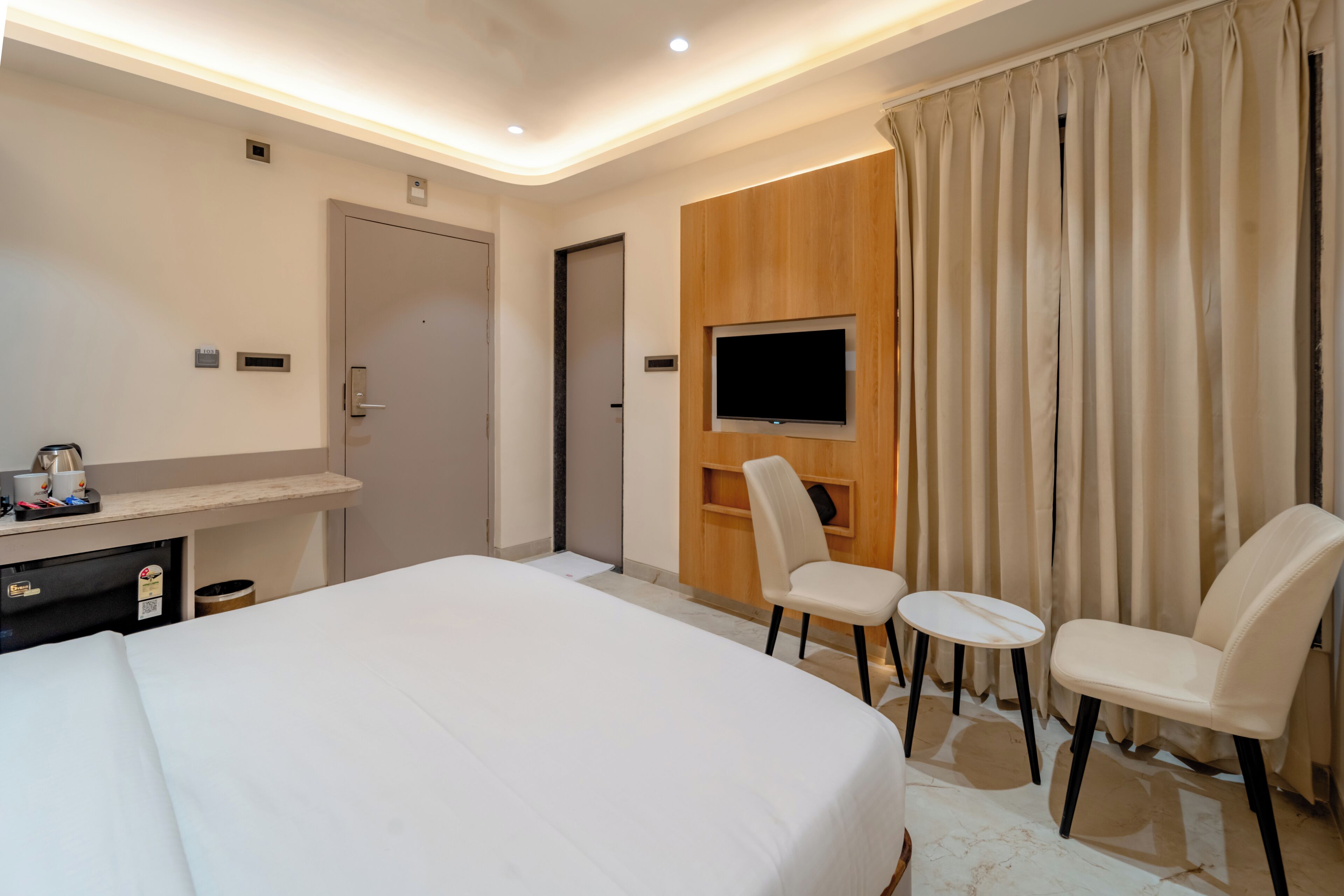 Een hotelkamer met een groot bed, een televisie bevestigd aan een houten paneel, een bureau met een stoel, en een bijzettafeltje.