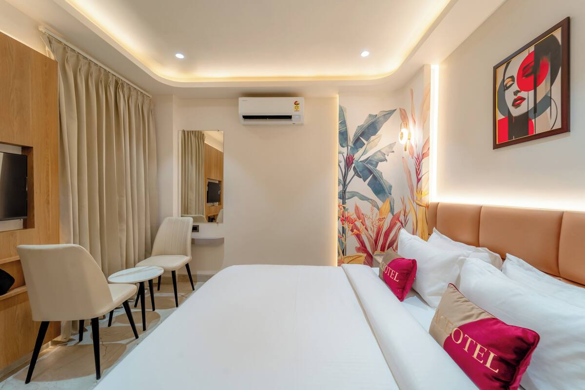 Quarto de hotel moderno com uma cama grande, TV, escrivaninha e uma cadeira.