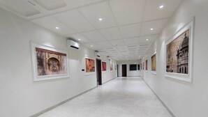 Un couloir aux murs blancs et au sol en marbre, orné d’œuvres d’art encadrées.
