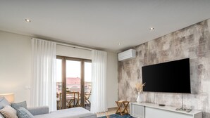 A modern living room with a large flat-screen TV mounted on a textured wall, a sofa, a coffee table, and a view of an outdoor balcony.