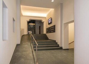 Una escalera con barandilla metálica que lleva a una plataforma con un televisor y una vitrina adosada a la pared.