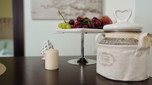 A table with a white ceramic plate holding grapes and cherries, a white candle, and a white ceramic jar with a heart-shaped lid. - B&B Alla Stazione (Palermo)