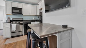 A modern kitchen with white cabinets, stainless steel appliances, and a large flat-screen TV mounted on the wall.