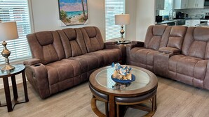 A living room with brown leather sofas, a glass coffee table, and a painting of a beach scene. - Oak Hill Waterfront Retreat – Unplug, Unwind, and Enjoy the Sunset (Oak Hill)