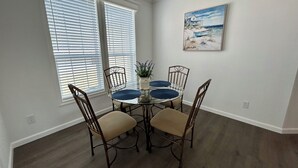 A dining area with a round glass table, four chairs, and a painting on the wall. - Oak Hill Waterfront Retreat – Unplug, Unwind, and Enjoy the Sunset (Oak Hill)