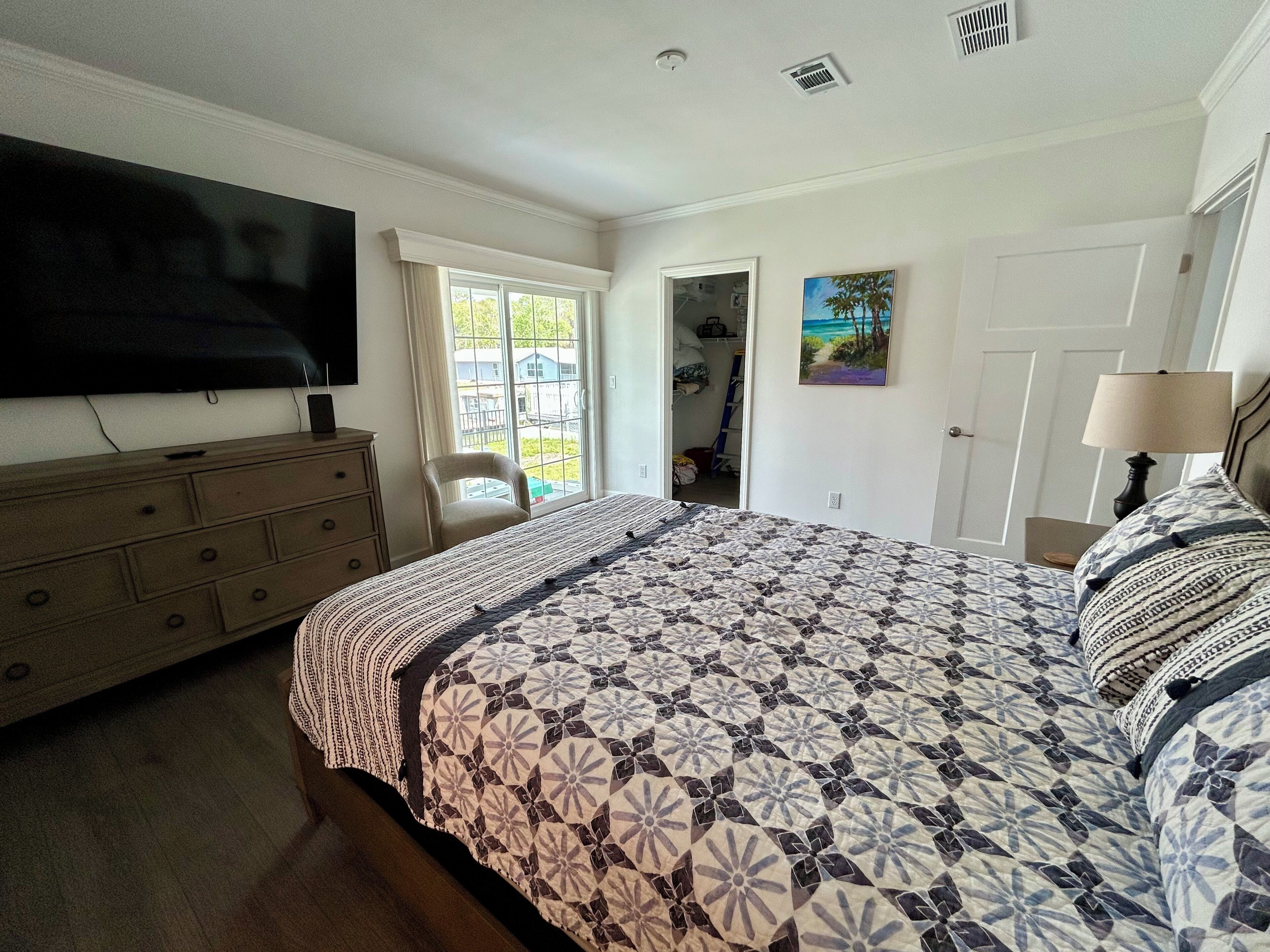 Quarto com cama grande, cômoda, televisão e janela com vista para o exterior.
