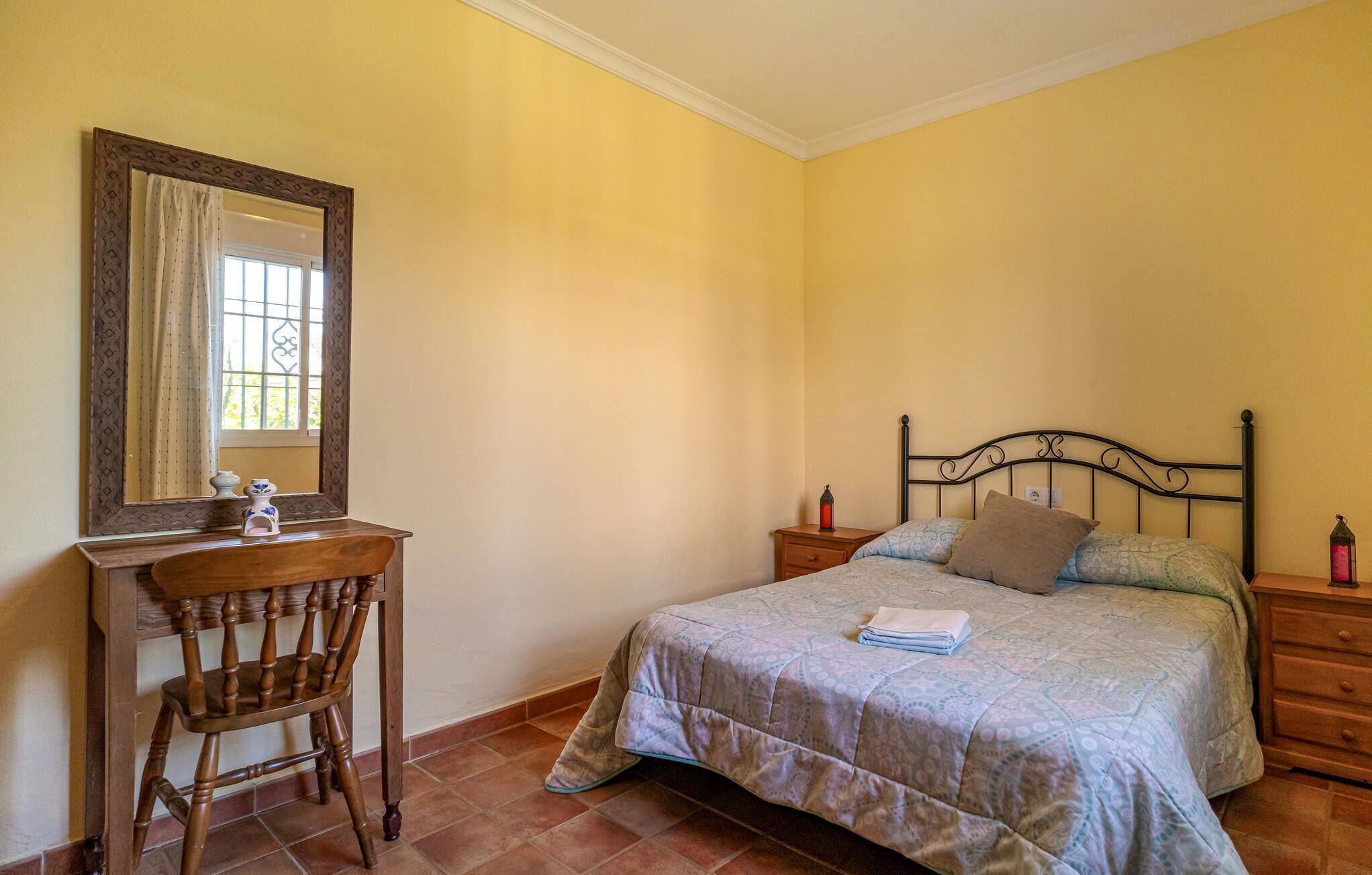 Une chambre à coucher avec un lit, une chaise en bois, une table de chevet et un miroir.