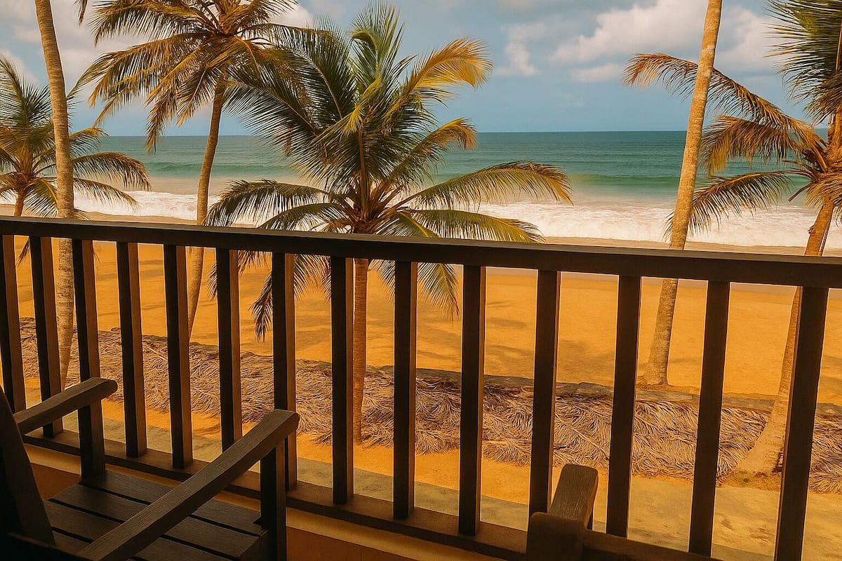 Une vue sur la plage depuis un balcon doté de balustrades en bois, avec des palmiers et les vagues de l’océan en toile de fond.