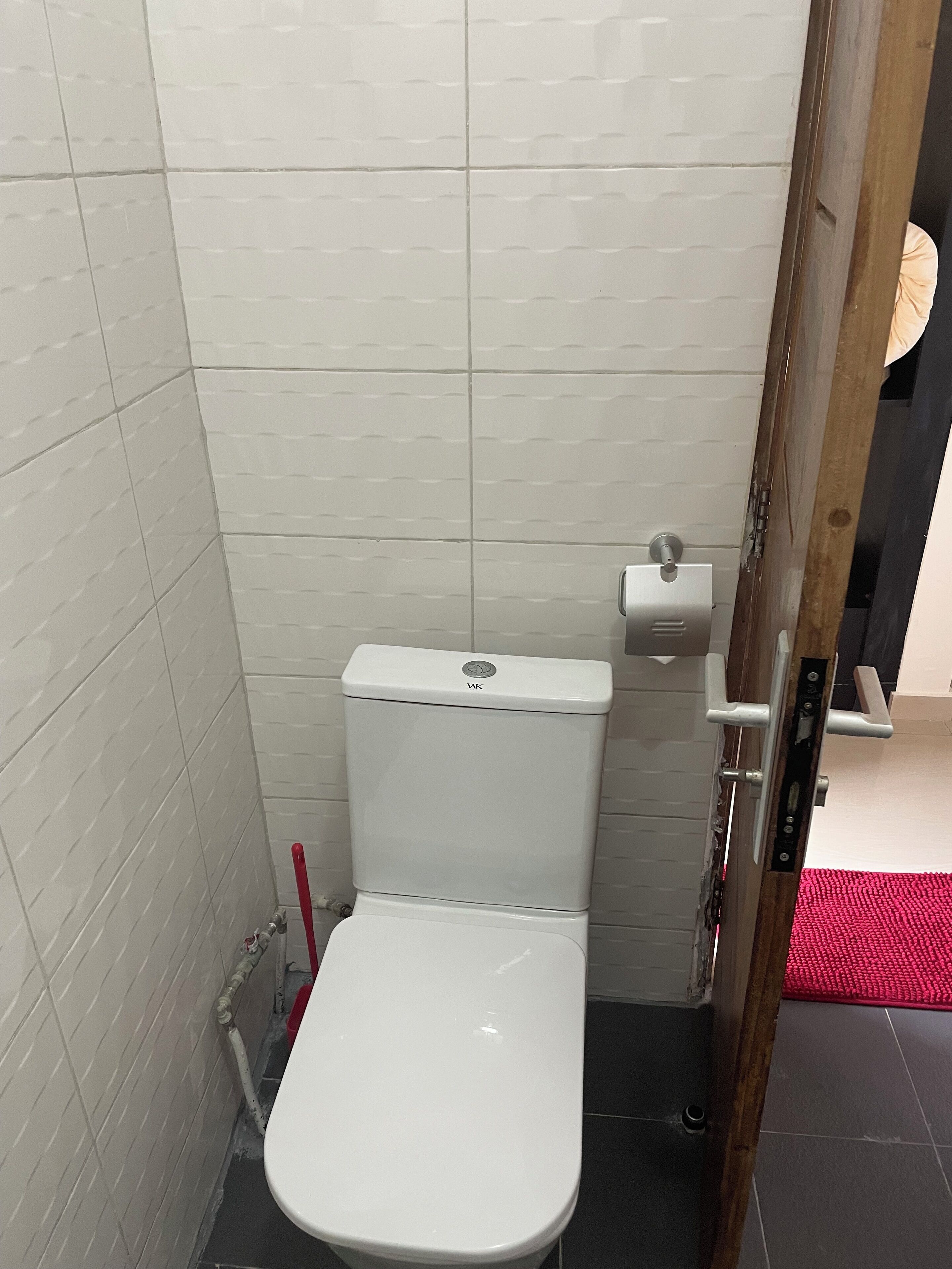 Un baño pequeño y cerrado con paredes de azulejos blancos y un inodoro blanco.