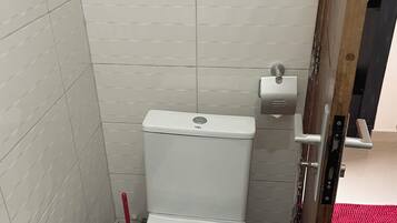 Un baño pequeño y cerrado con paredes de azulejos blancos y un inodoro blanco.