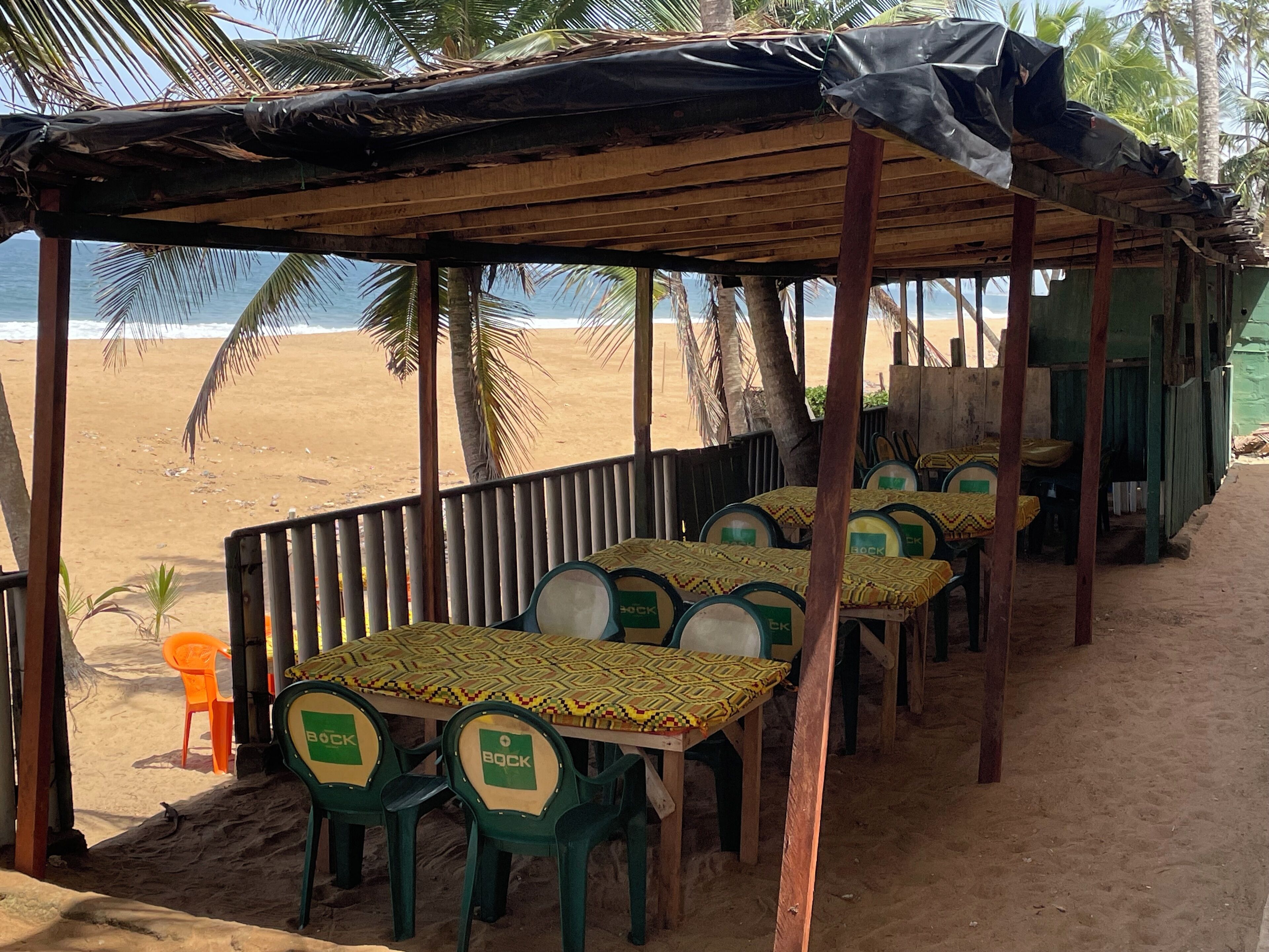 Un restaurante frente al mar con terraza al aire libre, que incluye mesas y sillas bajo un toldo de madera.