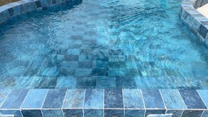 Une piscine dont le bord est revêtu de carreaux et dont l’eau est d’un bleu limpide.