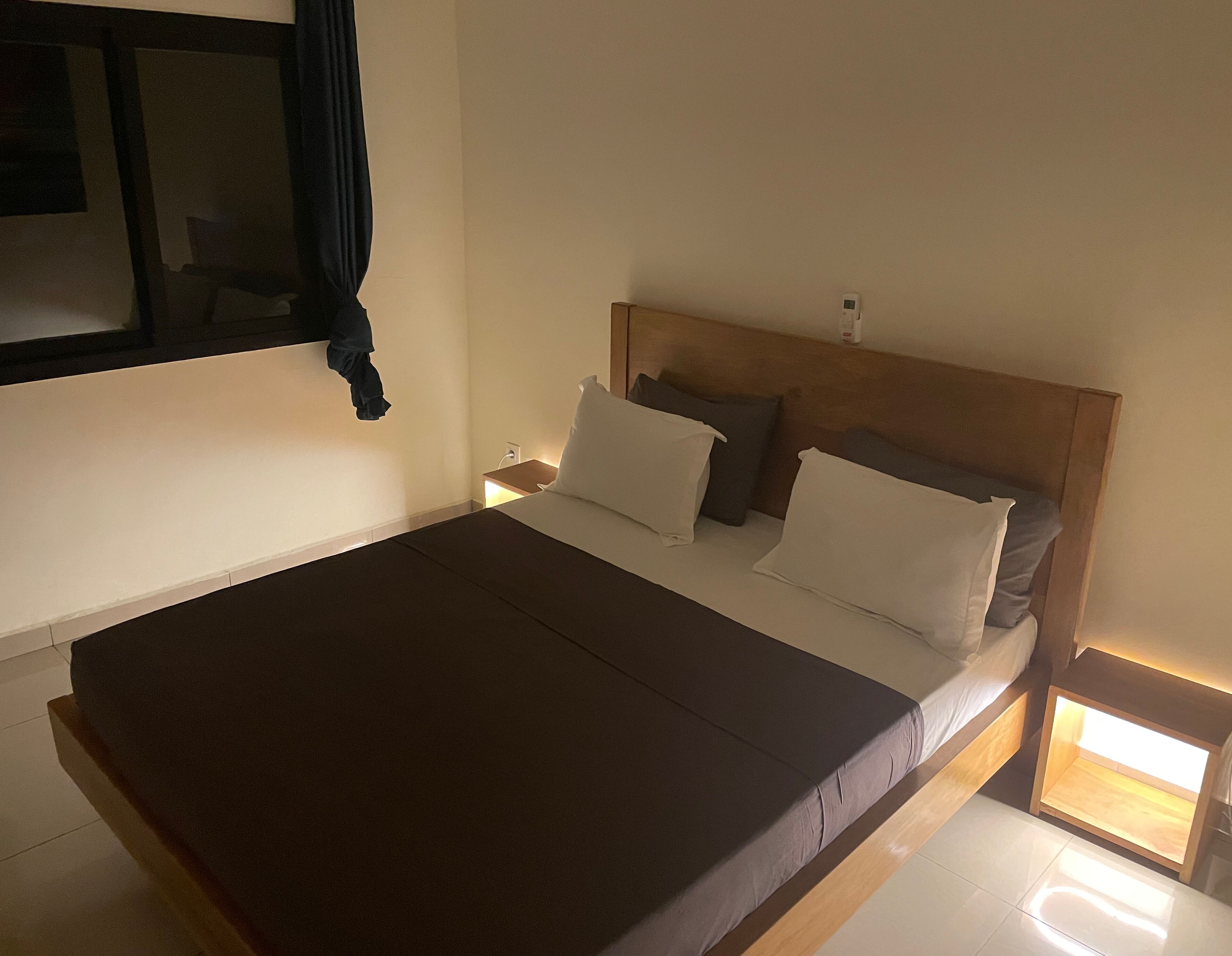 Un dormitorio con una cama grande, una mesita de noche y una ventana con cortinas.