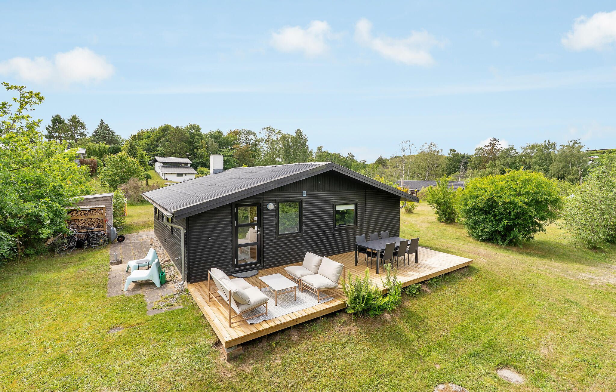 Eine kleine, dunkel gefärbte Holzhütte mit einer Veranda, einem Tisch und Stühlen.