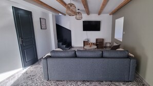 A modern living room with a grey sofa, a flat-screen TV, wicker pendant lights, and patterned floor tiles.