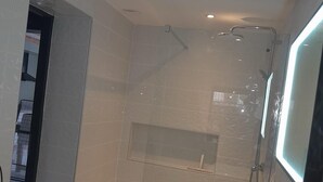 A modern bathroom with a glass-enclosed shower, a white sink, and a mirror with a light.