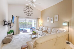 Un salon comprenant un canapé, une table basse, un ventilateur de plafond, une horloge et une vue sur l’extérieur.