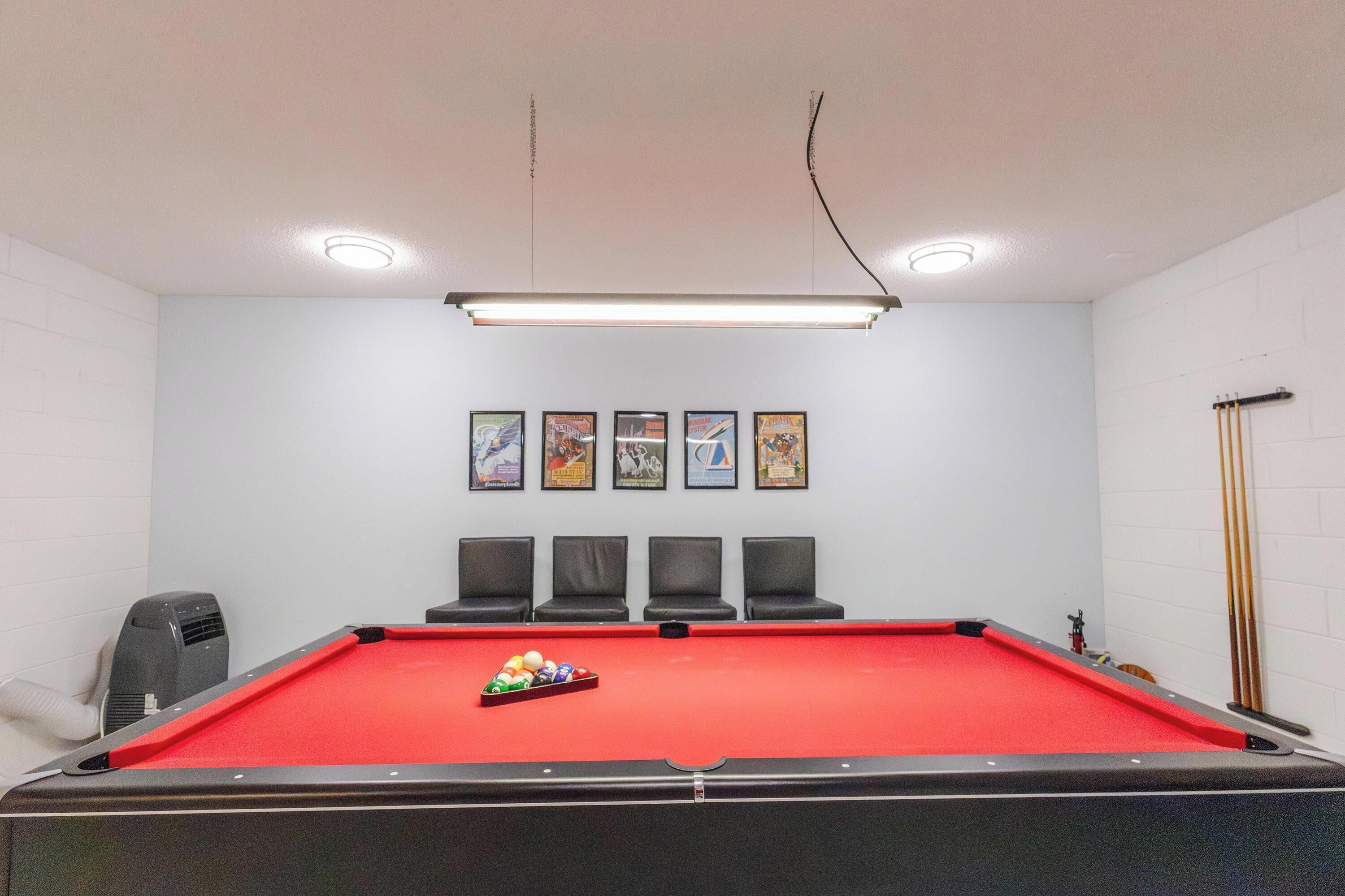 A pool table with chairs, a heater, and framed pictures on the wall.